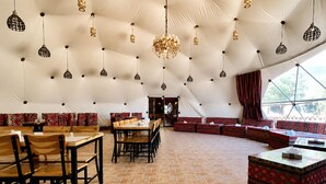 A tented dining area with tables and benches, a patterned floor, and hanging light fixtures. - Hasan Zawaideh Camp (Wadi Rum)