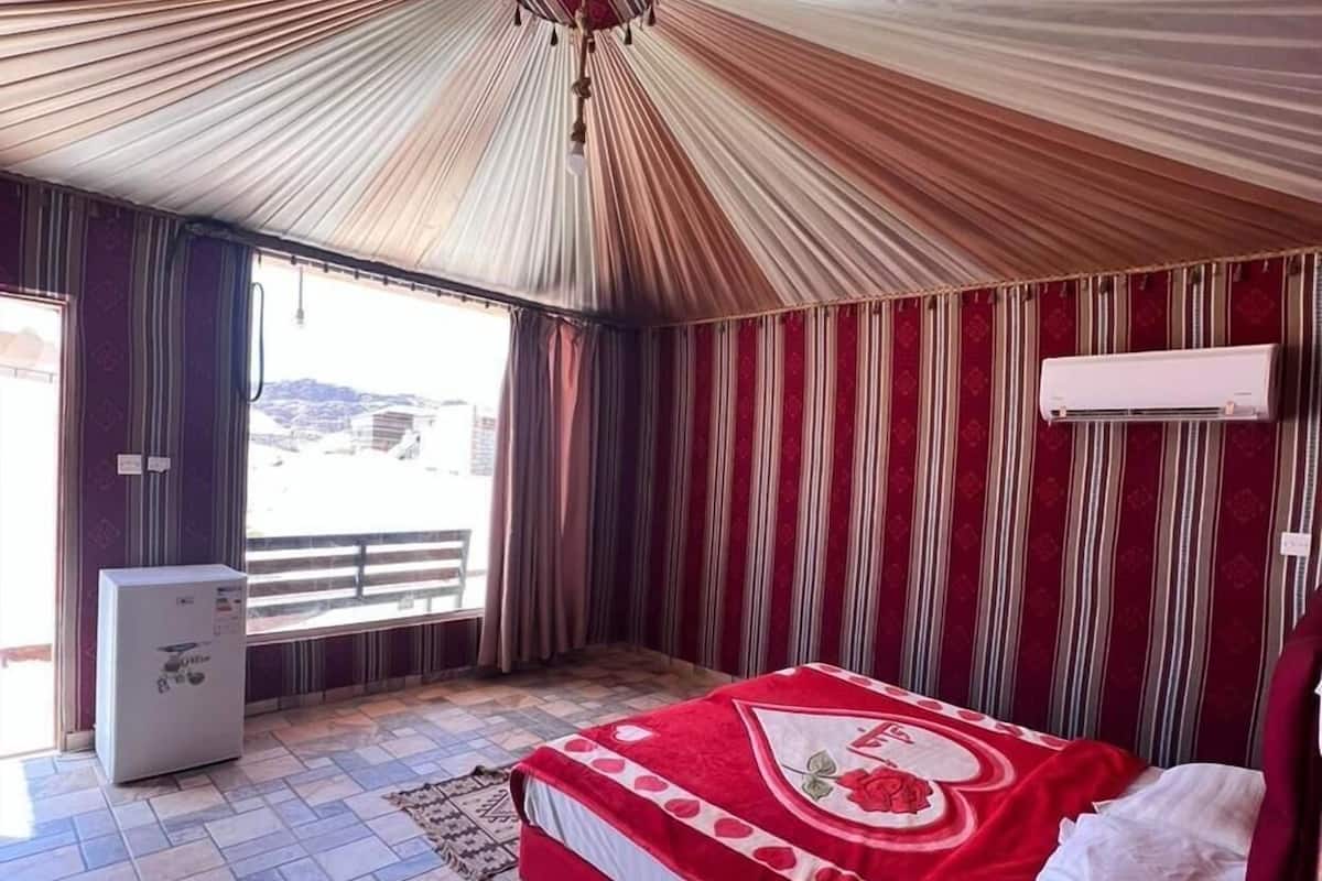 A room with a bed, a small refrigerator, a window, and a ceiling fan.