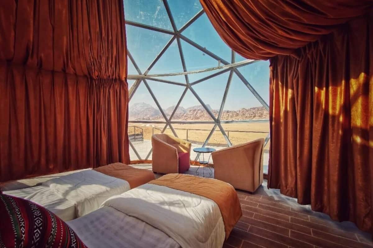 A room with two beds, a view of a desert landscape through a large window, and red curtains.