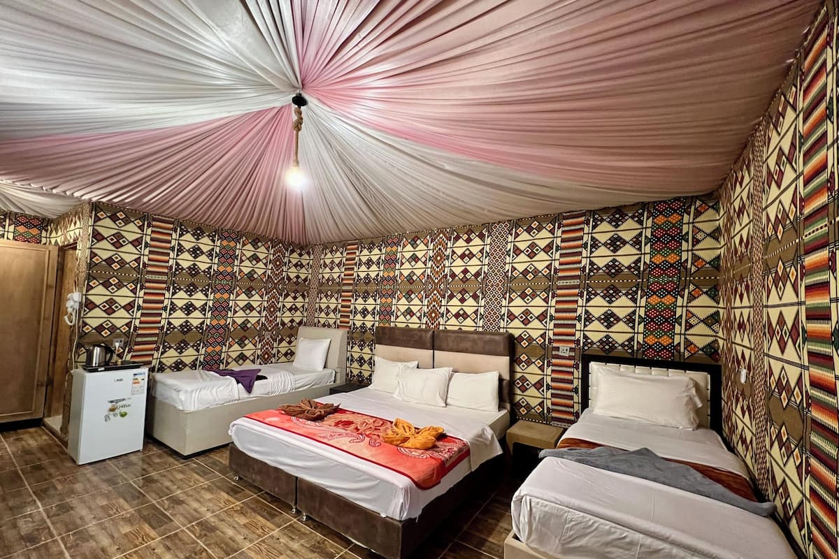 A room with a patterned wall, a bed, a sofa, and a small table with a kettle.