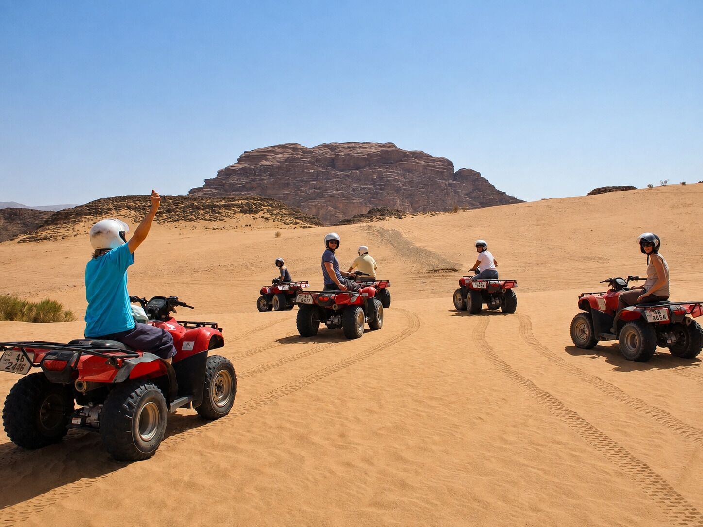 A group of people on ATVs in a desert with a large rock formation in the background.