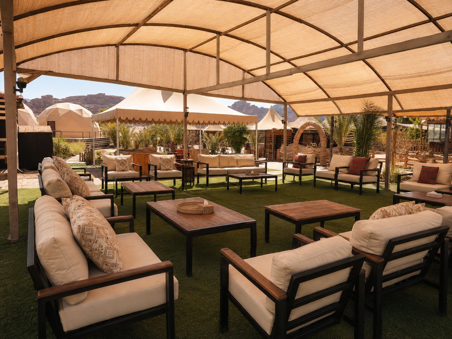 An outdoor seating area with multiple sofas and tables, shaded by large canopies.