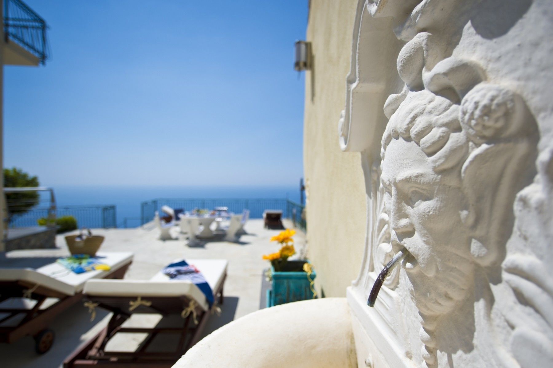 A terrace with lounge chairs and tables overlooking the sea.