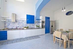 A modern kitchen with blue and white cabinetry, a built-in oven, and a dining area with wicker chairs.