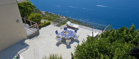 A rooftop terrace with a round table and chairs, overlooking a coastal view.