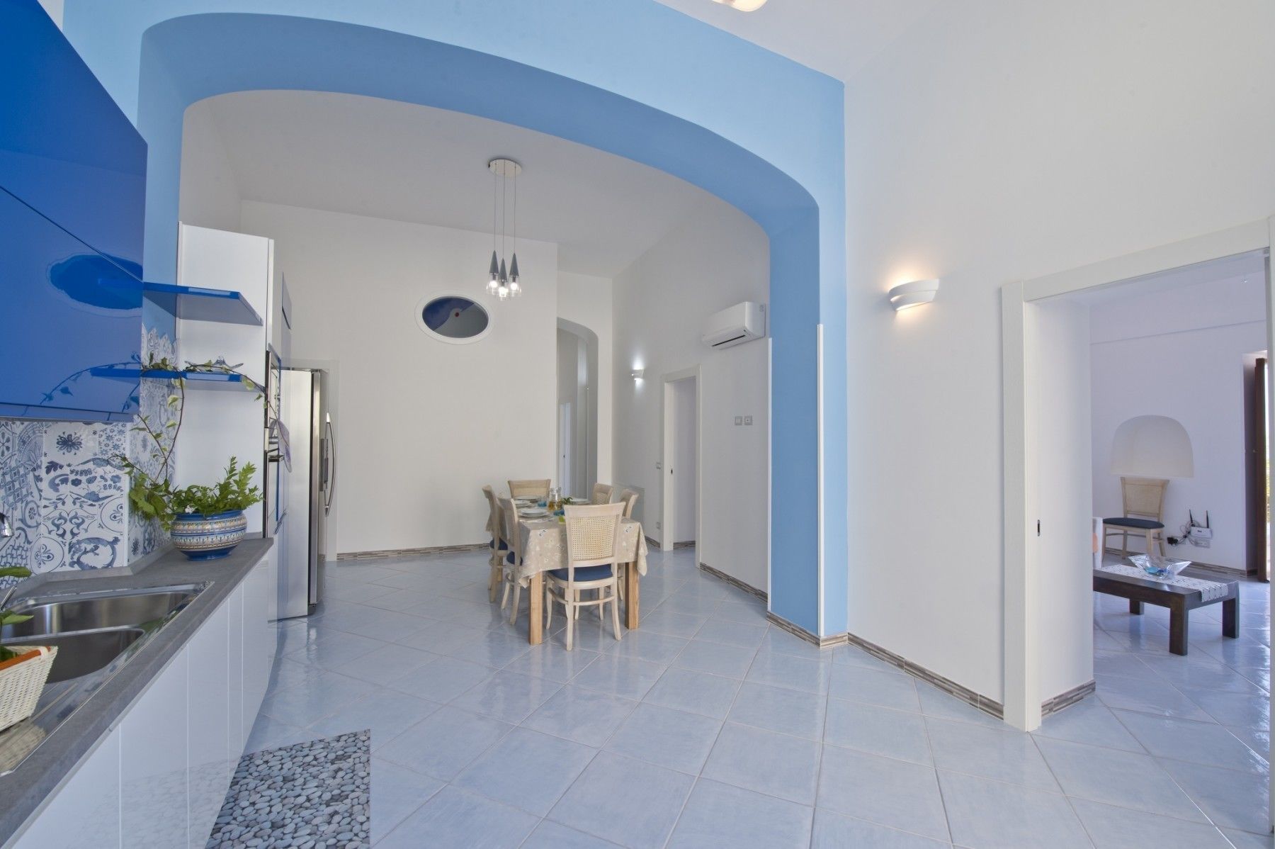 A spacious living area with a dining table, chairs, and a kitchen area with a refrigerator and sink.