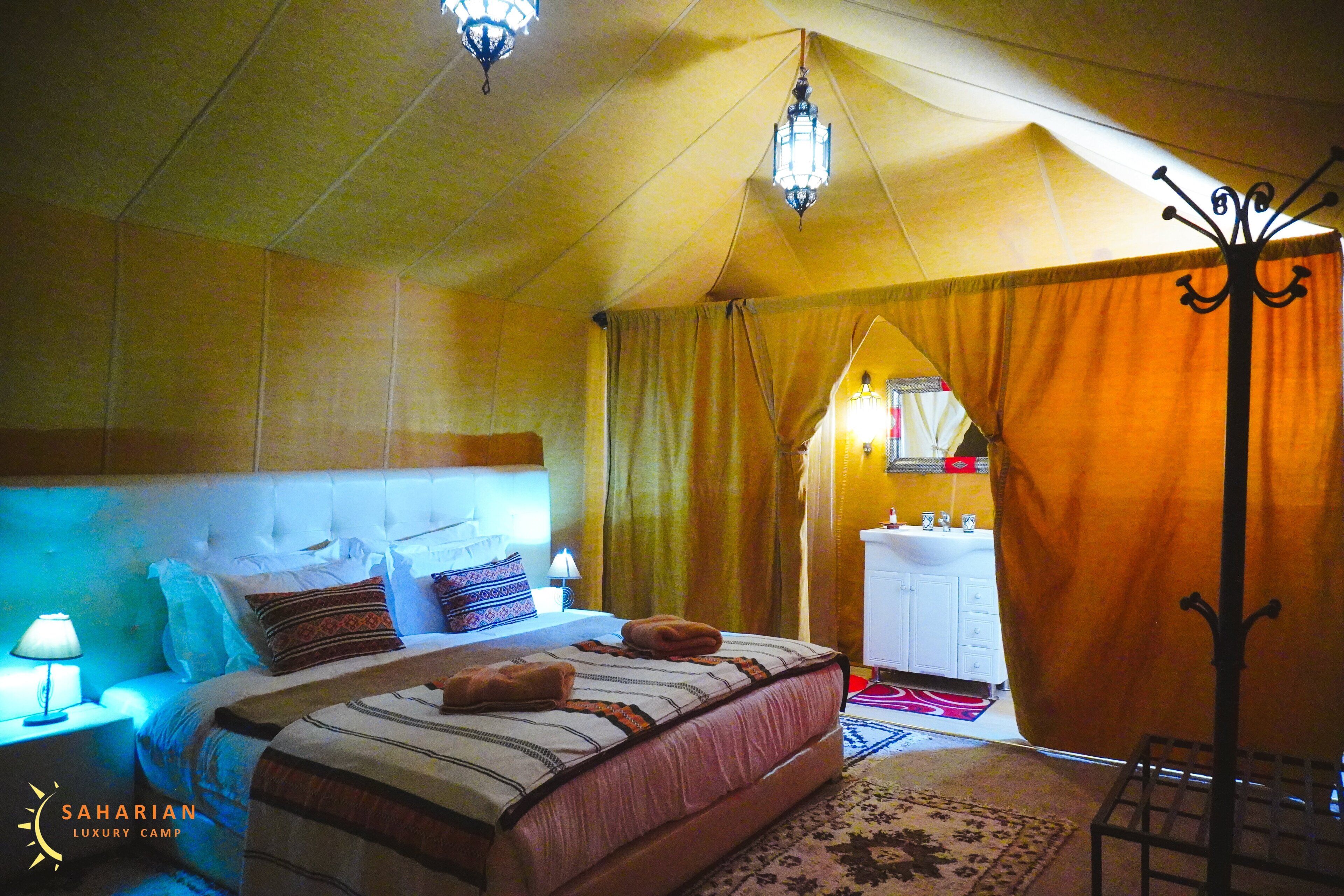 Habitación de lujo con carpa, cama, lámpara de noche y baño visible a través de una cortina.
