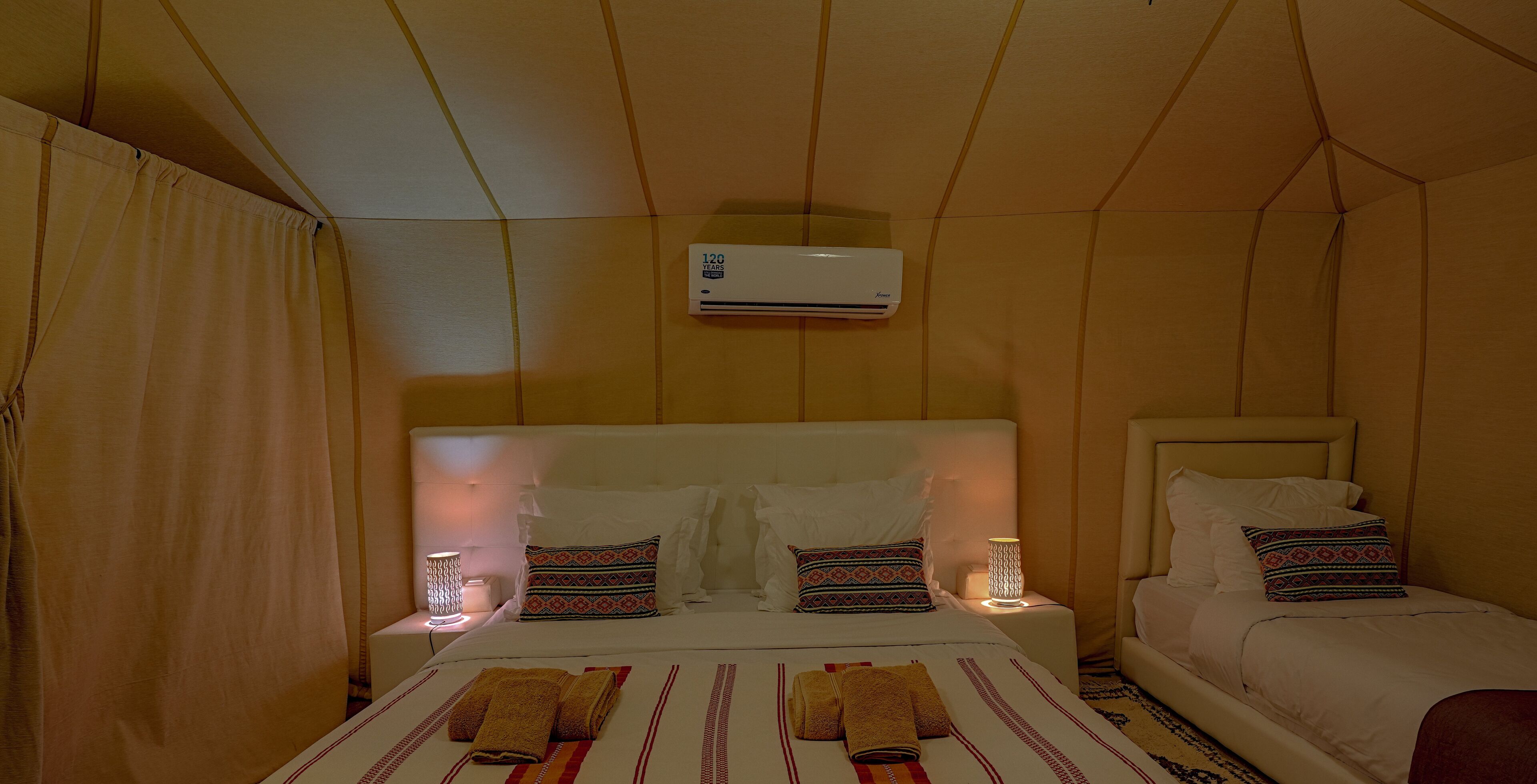 A hotel room with a bed, two bedside tables, an air conditioner, and a night lamp.