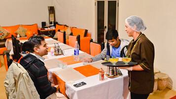A conference room with a long table, orange cushions, and a person serving food.