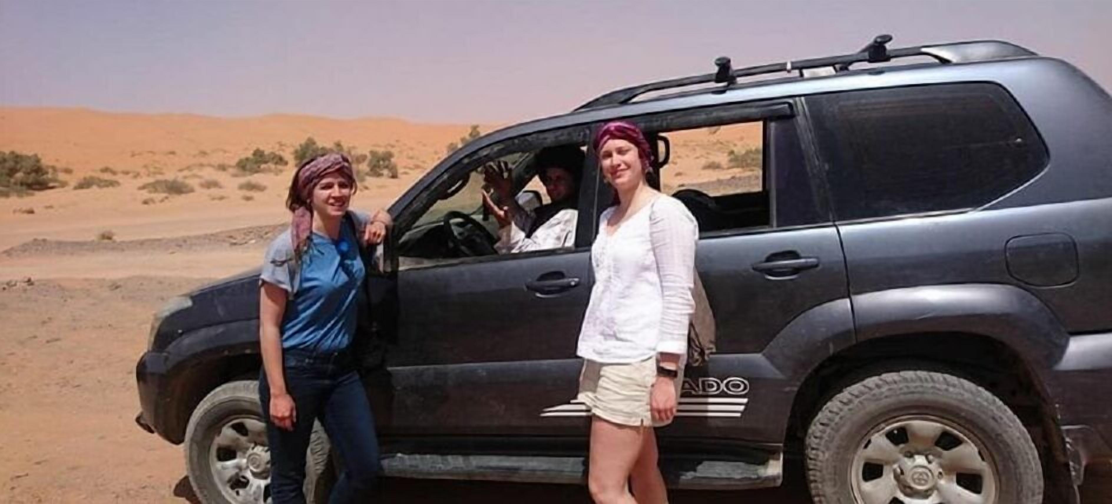 Un vehículo estacionado en el desierto con dos personas a su lado.