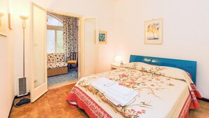 A hotel room with a bed, a chair, a small table, and a window with curtains.