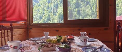 A dining table set with various dishes and cups, a window with a forest view, and wooden walls.
