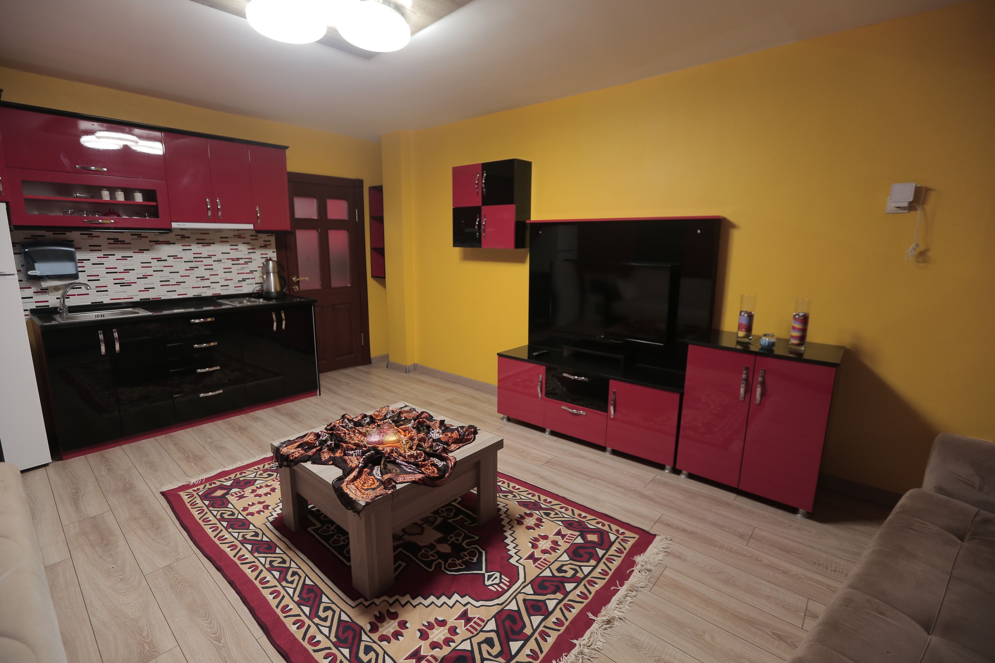 A modern kitchen with red cabinets, a black refrigerator, and a patterned rug.