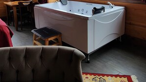 A cozy room with a wooden ceiling, a large window with curtains, a bathtub, a small stool, and a patterned rug. - Ayder Suit (Camlihemsin)