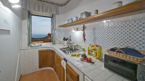 Uma cozinha com paredes revestidas de azulejos brancos, uma janela com vista, armários de madeira, fogão e micro-ondas.