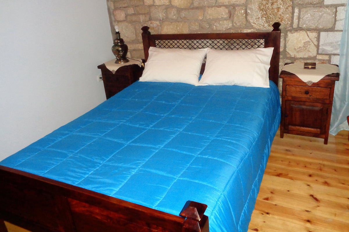 Ein Bett mit blauer Decke, einem Holz-Kopfteil und einer Steinwand dahinter.