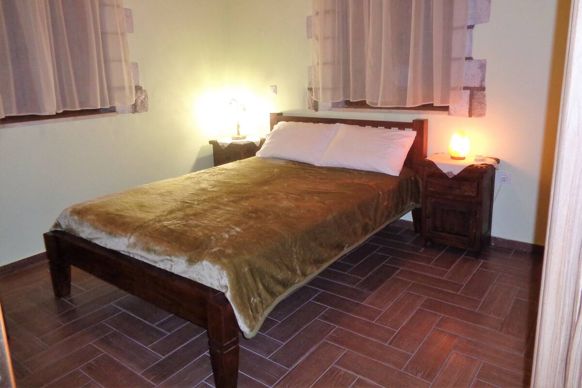 Ein Schlafzimmer mit einem hölzernen Bett, zwei Nachttischen mit Lampen und einem Parkettboden mit Zickzackmuster.