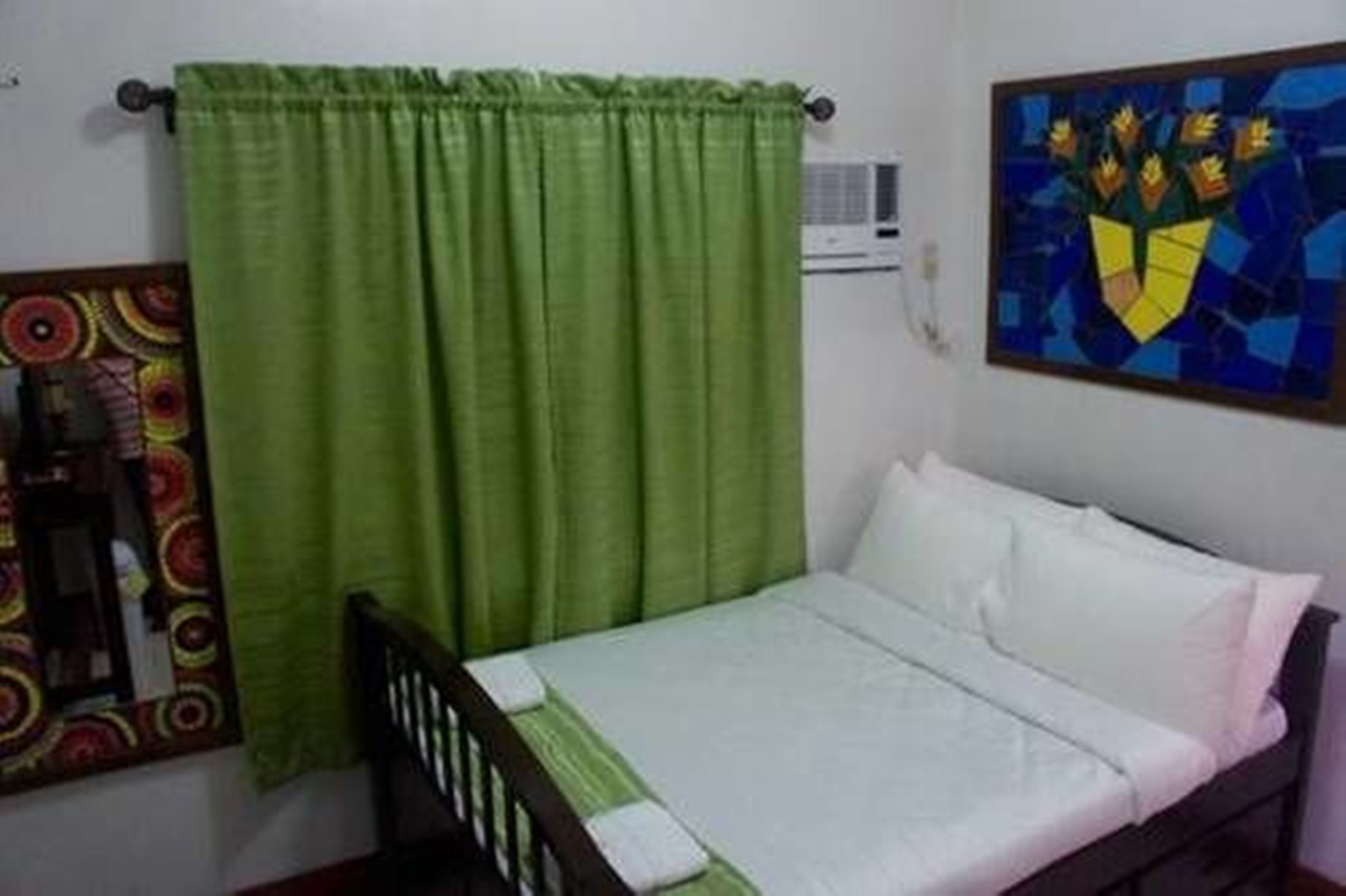 A single bed with white bedding in a room with a green curtain and a colorful painting on the wall.