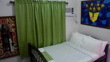 A single bed with white bedding in a room with a green curtain and a colorful painting on the wall.