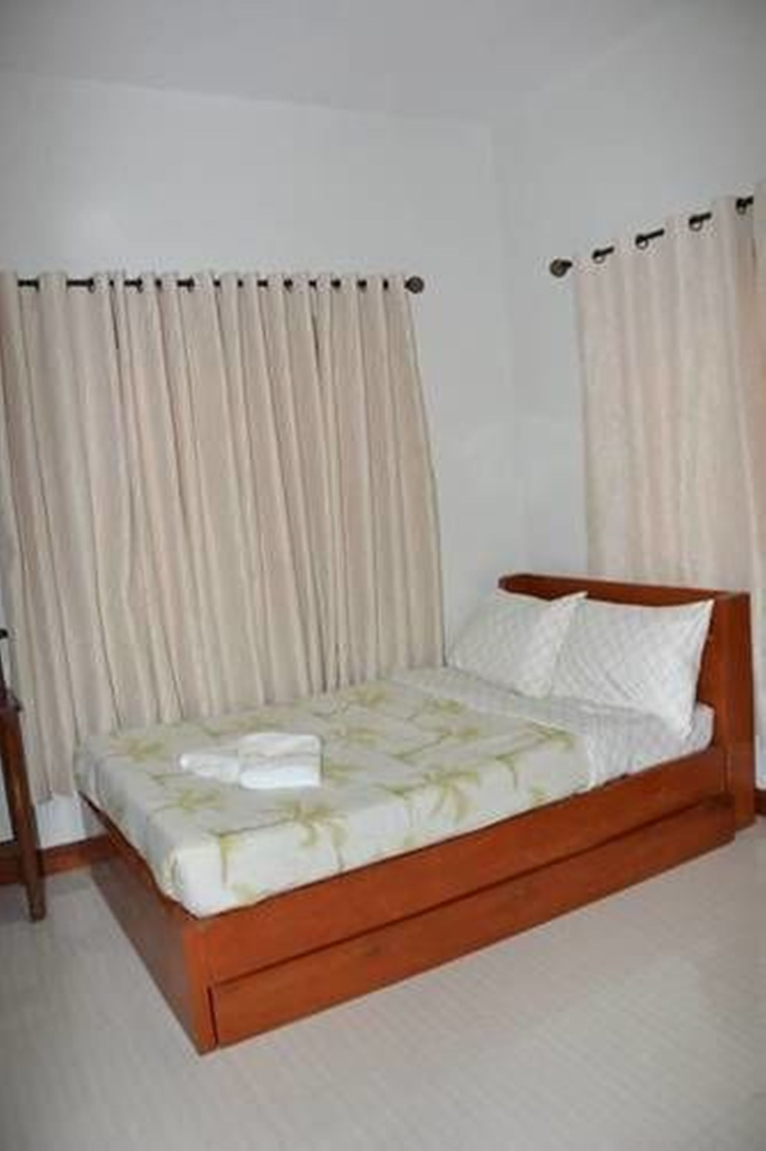 Una cama individual con estructura de madera y ropa blanca, cortinas a ambos lados y una pared lisa.