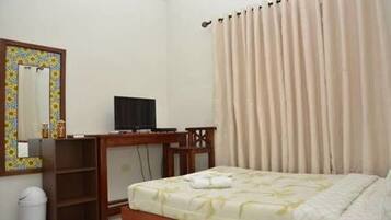 A hotel room with a bed, a desk with a computer, a chair, a mirror, and a window with curtains.