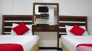 Ein Hotelzimmer mit zwei Betten, jeweils mit weißer Bettwäsche und roten Kissen. Es gibt ein Holz-Kopfteil, eine kleine, hölzerne Kommode mit Schubladen und einen Flachbildfernseher, der über der Kommode angebracht ist.
