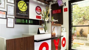 Ein Hotelrezeptionstisch mit einem großen Schild mit dem Schriftzug 'YOYO', gerahmten Zertifikaten und einem Schild mit der Aufschrift '100% Kundenzufriedenheit garantiert'.