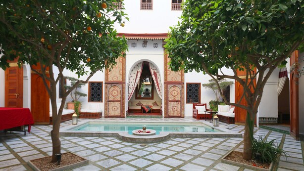 A courtyard with a pool, seating areas, and a view of a building with ornate doors and windows. - Riad Zineb (Marrakech)