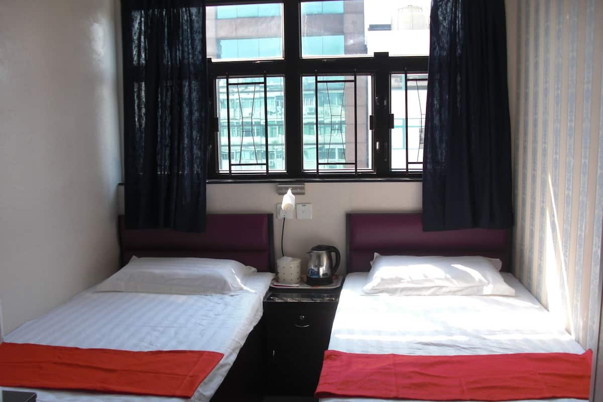 A hotel room with two single beds, a nightstand with a kettle, and a window with curtains.