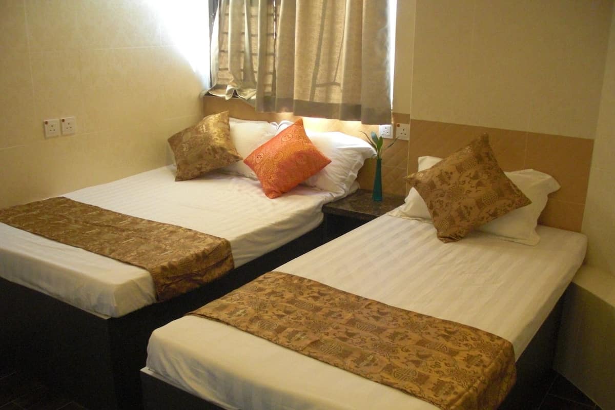 Two single beds with patterned bedspreads, a window with curtains, and a wall socket.