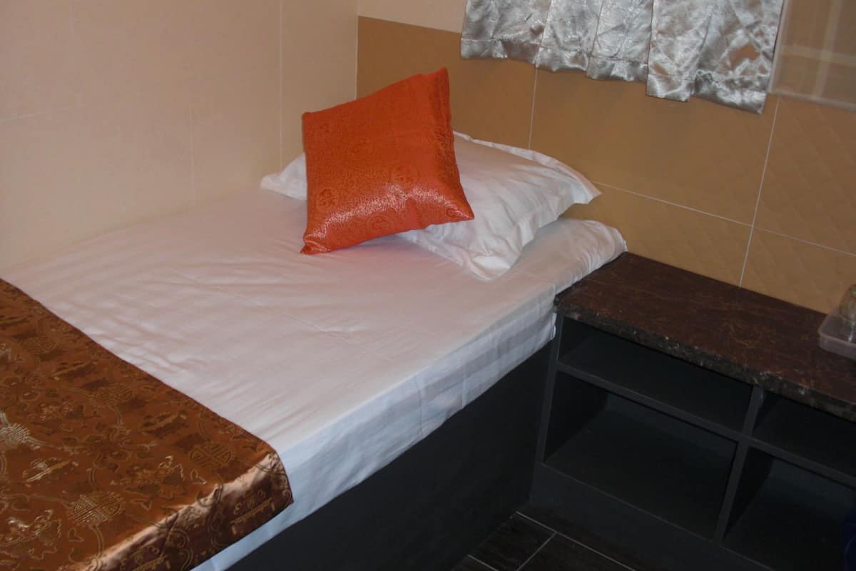 A small, neatly made bed with white linens and a single orange pillow.