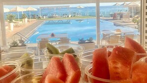 En vy över ett område vid poolen med fri sikt över havet, en pool och ett buffébord med frukt.