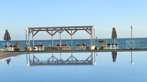 En vacker, turkosblå pool med en pergola och stolar, med utsikt över havet.