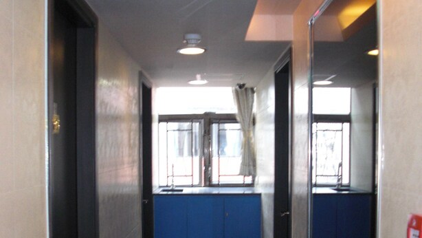 A corridor with a blue counter, a fire alarm, and a door on the left. - Empire Commercial Hotel (Kowloon)