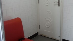 A room with a red chair, a white door with decorative swirls, and a tiled floor. - Empire Commercial Hotel (Kowloon)