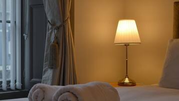 A neatly made bed with rolled towels, a bedside lamp, and a window with curtains.