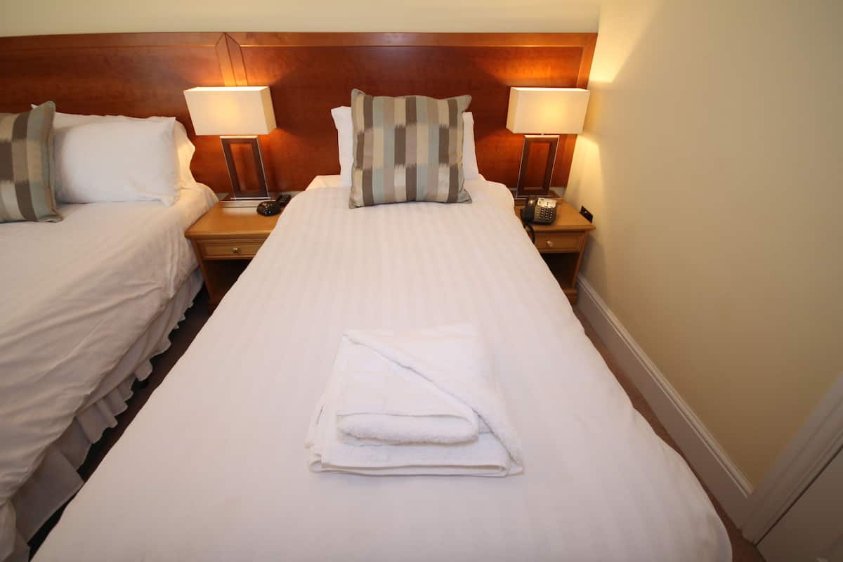 Habitación de hotel con dos camas, cada una con una almohada, una lámpara de noche y una toalla doblada sobre la cama.