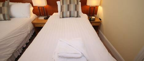 A hotel room with two beds, each with a pillow, a bedside lamp, and a folded towel on the bed.