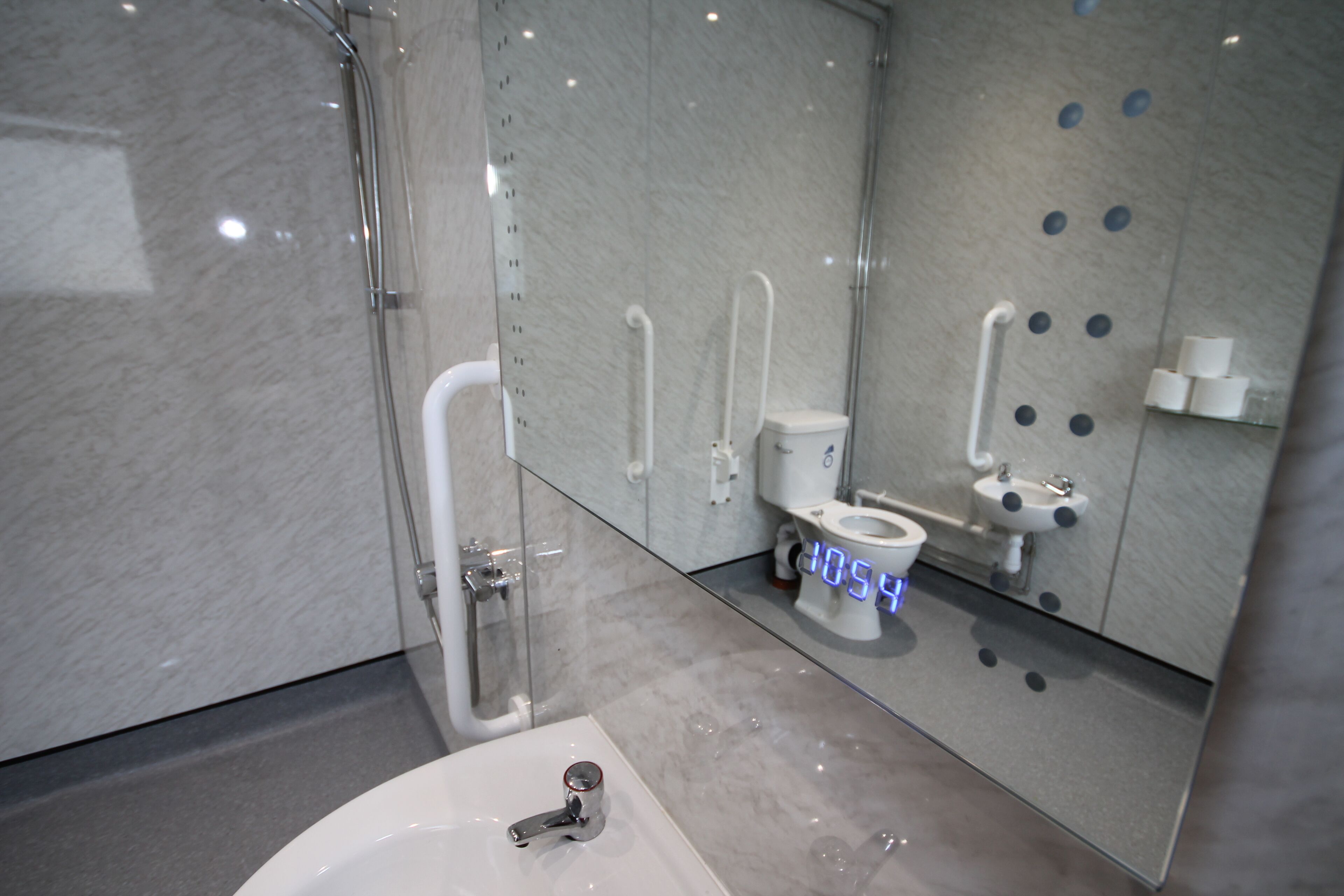 A modern bathroom with a glass-enclosed shower, a white toilet, and a sink with a digital display.