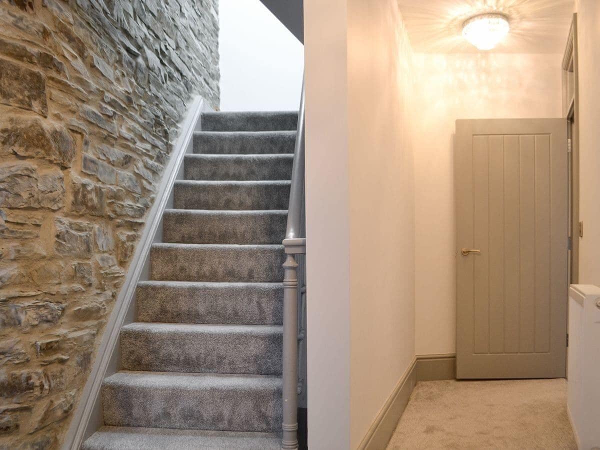 Una escalera con alfombra, un muro de piedra en un lado y una puerta al final.