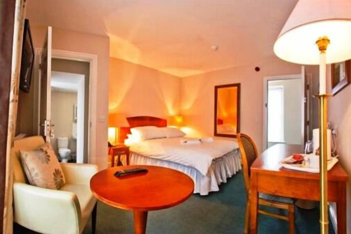Una habitación de hotel con cama, escritorio, silla, mesa y lámpara.