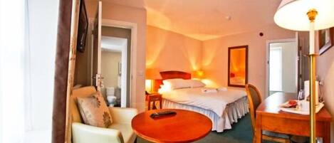 A hotel room with a bed, a desk, a chair, a table, and a lamp.