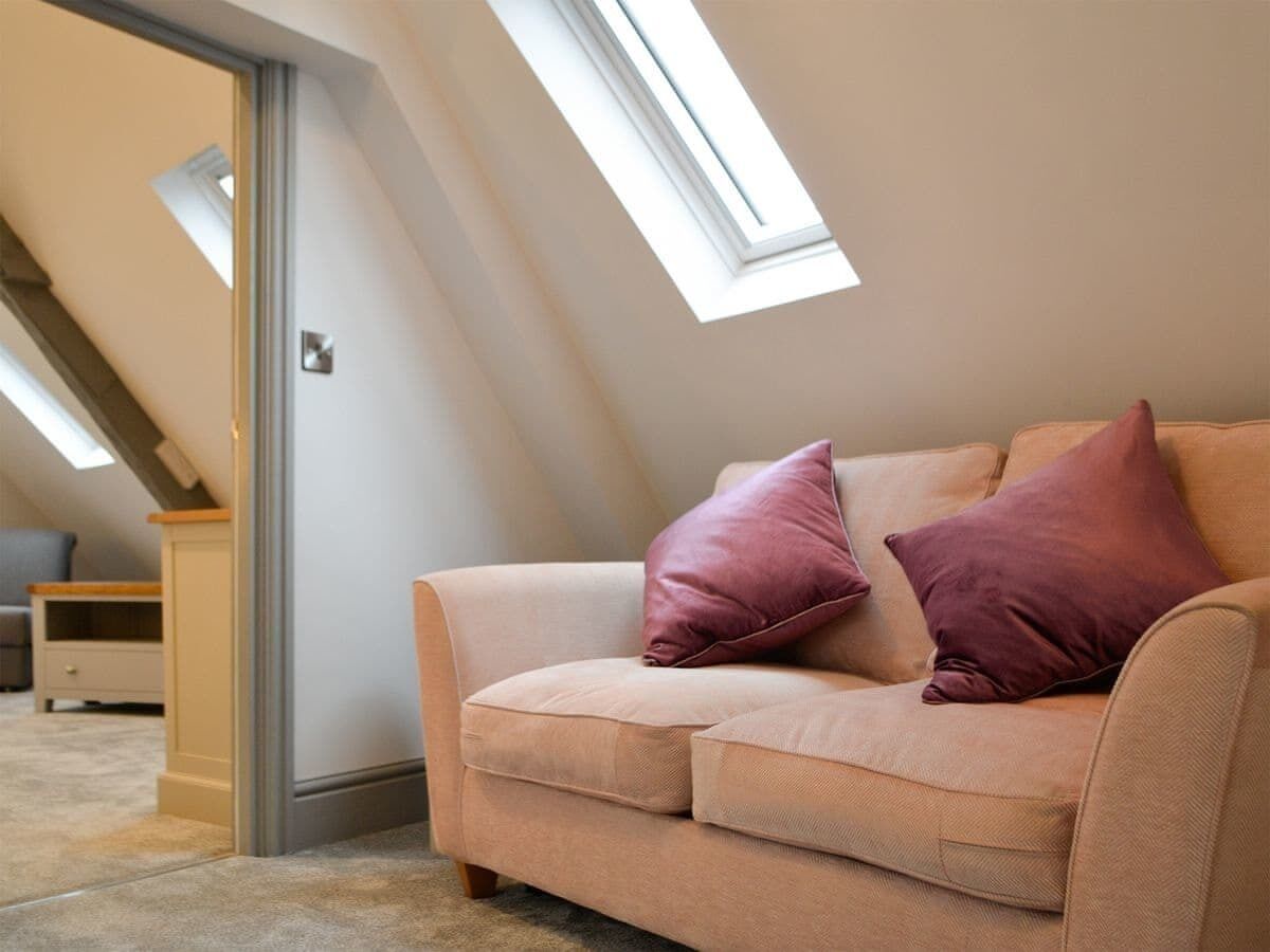 A beige sofa with two pillows in a room with sloped ceilings and skylights.