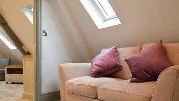 A beige sofa with two pillows in a room with sloped ceilings and skylights.