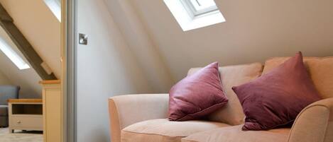 A beige sofa with two pillows in a room with sloped ceilings and skylights.