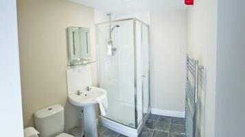 Un baño con cabina de ducha de vidrio, un lavamanos blanco y un inodoro.