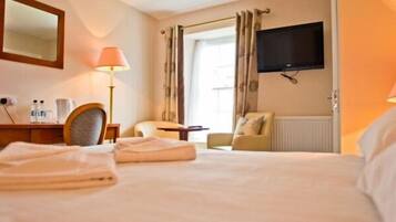A hotel room with a bed, a desk with a lamp, a chair, a television, and a window with curtains.