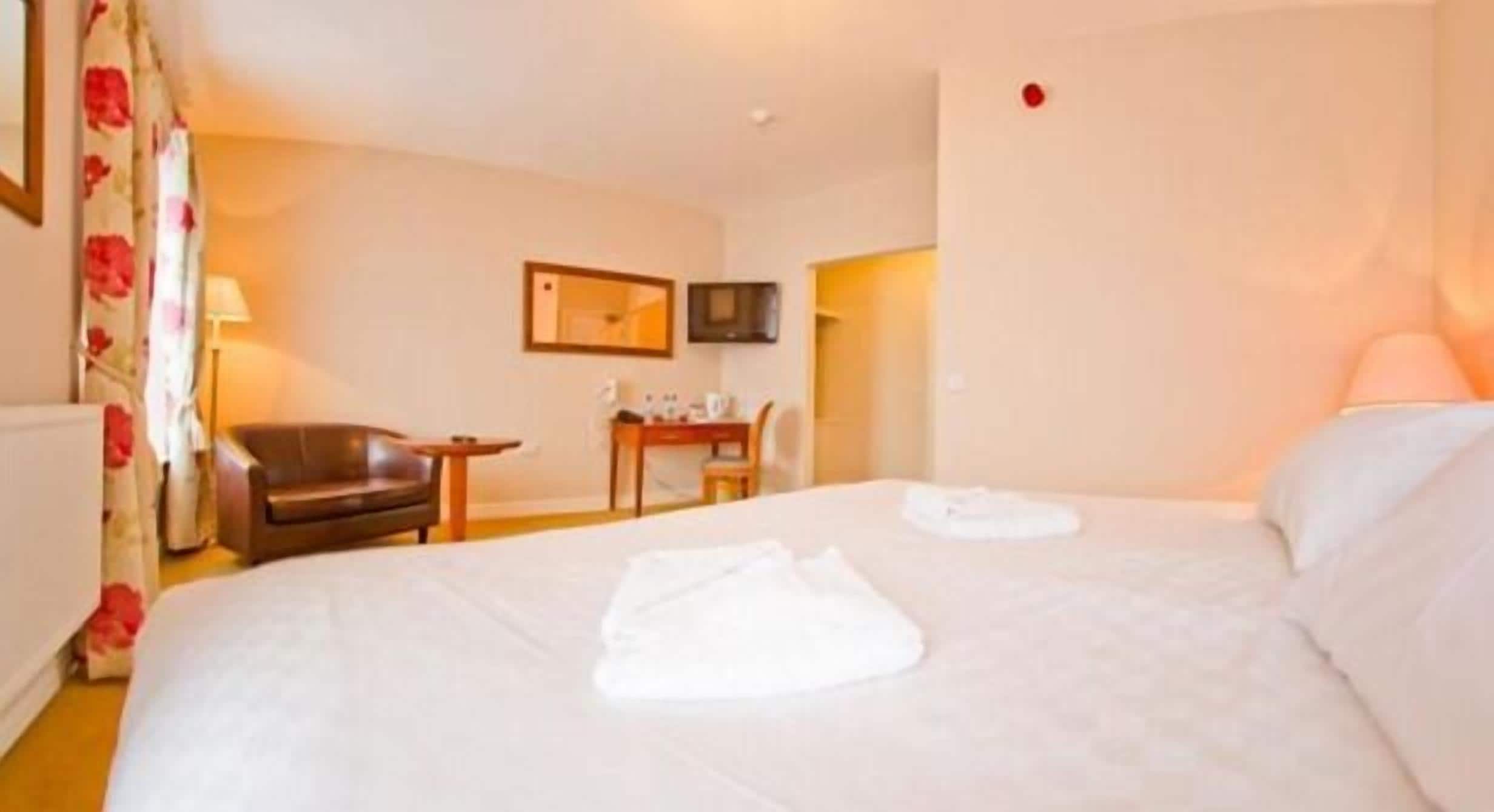 Quarto de hotel com uma cama, uma cadeira, uma mesinha e uma televisão.