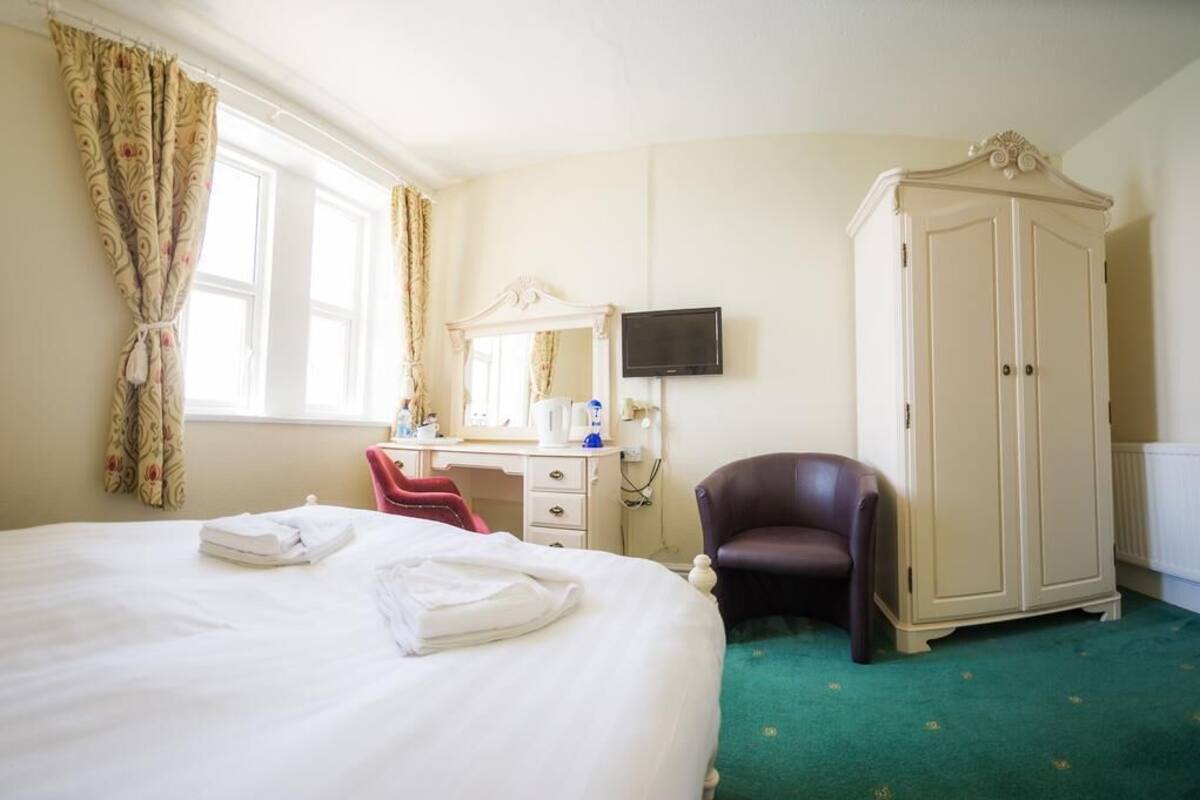 A hotel room with a bed, a desk with a mirror, a television, a wardrobe, and a chair.