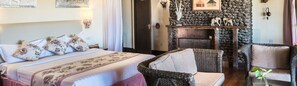 A bedroom with a bed, two chairs, a fireplace, and a stone wall.